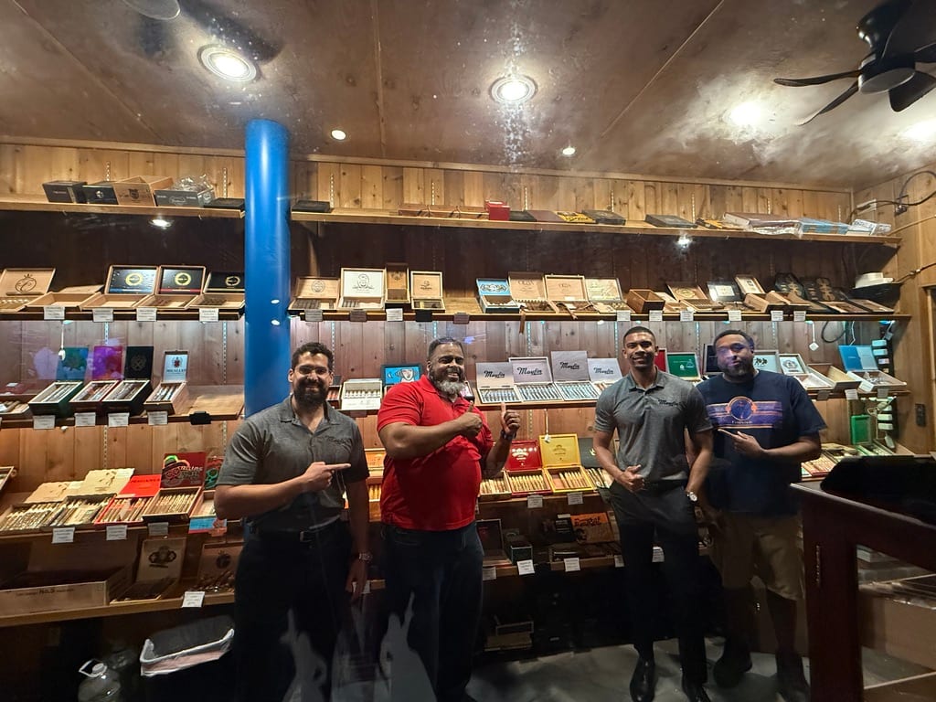 Mayfin team members with a lounge partner in front of a cigar wall